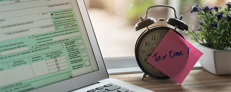 Tax time sticky note reminder on clock in front of digital tax form on laptop screen