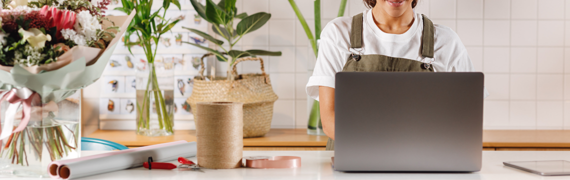 Florist shop employee working at a laptop, a bouquet of flowers off to the side